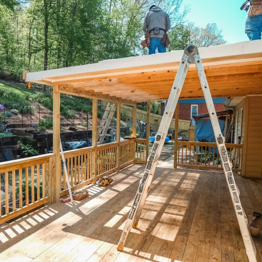 Deck installation contractor in Hoover building a covered wood deck with new railing and roof framing, showing workers and ladders during the construction process